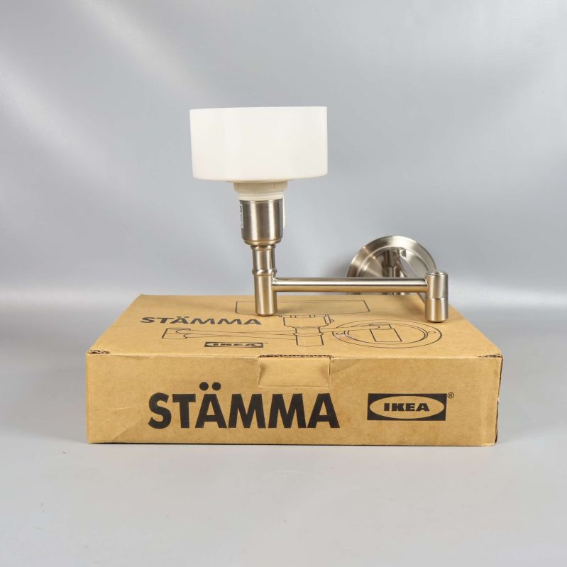 Vägglampa med vit skärm och metallarm står på STÄMMA-låda
