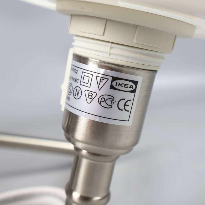 Närbild på etikett med IKEA-symbol på metallarm vid lampsockel