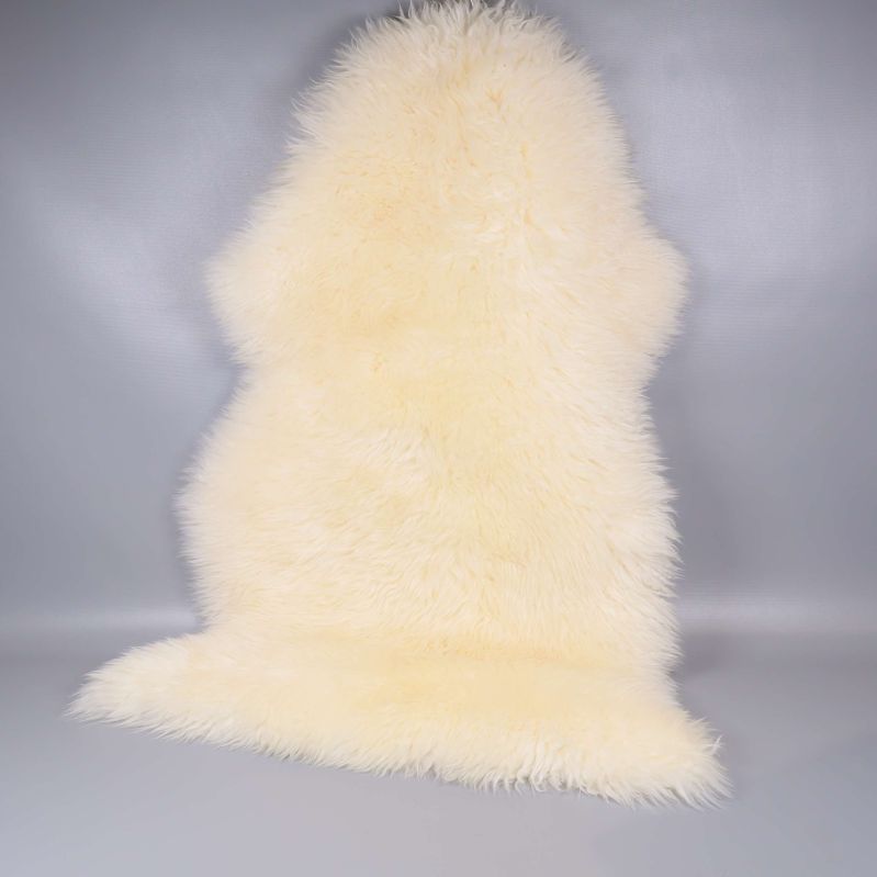 Långhårigt vitt fårskinn i helbild mot grå vägg