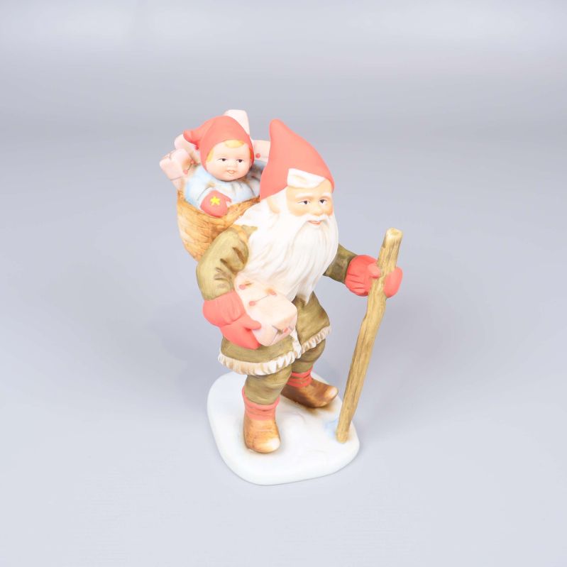 Tomtefigur med vandringsstav och barn i korg på ryggen