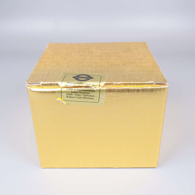Gyllene ask med etikett tillhörande porslinsfigur