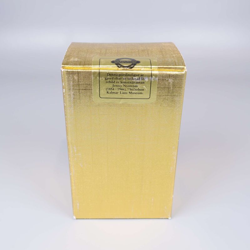 Guldfärgad produktkartong till tomtefigur med etikett på ovansidan