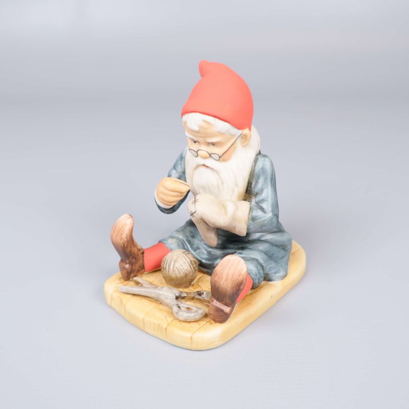 Tomtefigur sittande med röd luva och blå dräkt