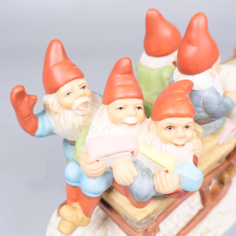 Närbild på tre tomtar sittande på släden i porslin