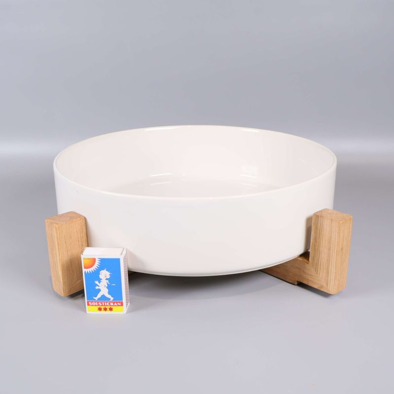 Vit skål i träställning bredvid en tändsticksask för storleksjämförelse