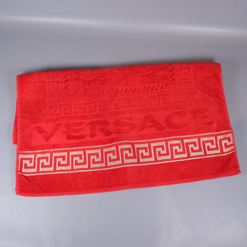 Utbredd röd handduk med VERSACE-text och guldfärgad bård
