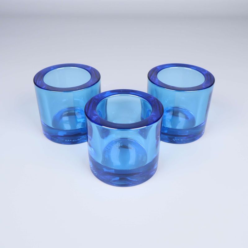 Tre ljuslyktor i blått glas uppställda i en triangel på vit bakgrund