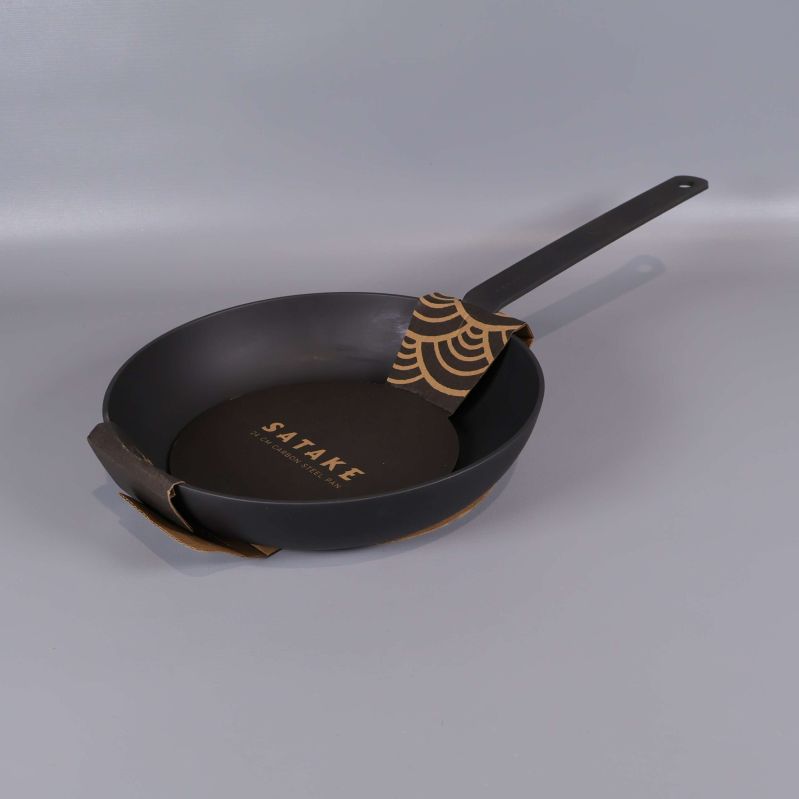 Mattsvart kolstålspanna med långt handtag på grå bakgrund