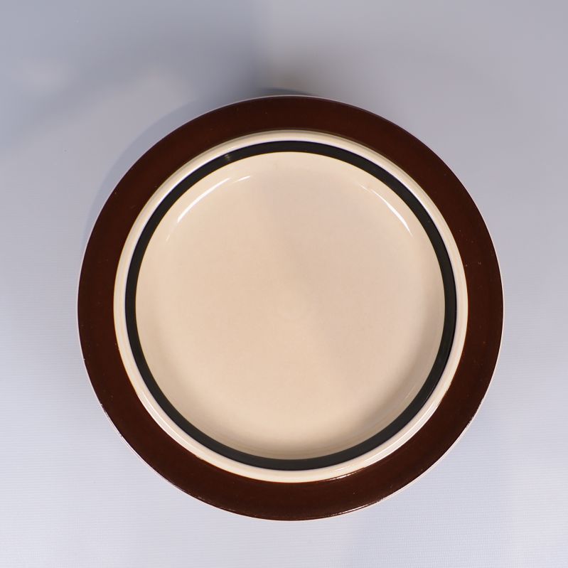 En tallrik med bred brun kant och beige mitt ovanifrån