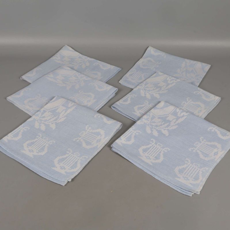 Sex ljusblå och vita linneservetter utlagda på ett bord