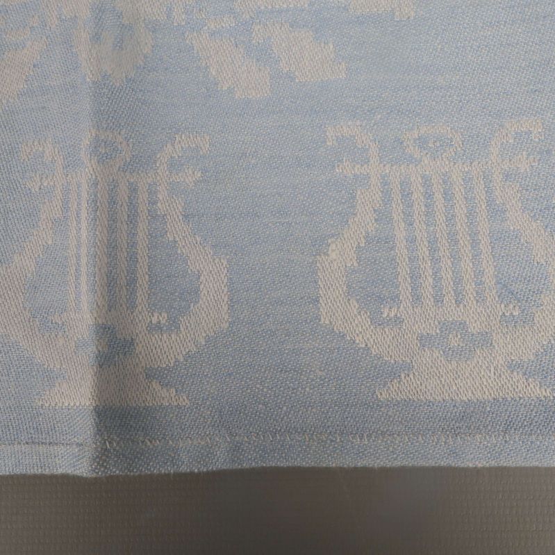 Närbild av servettkant med lyra-motiv i väven