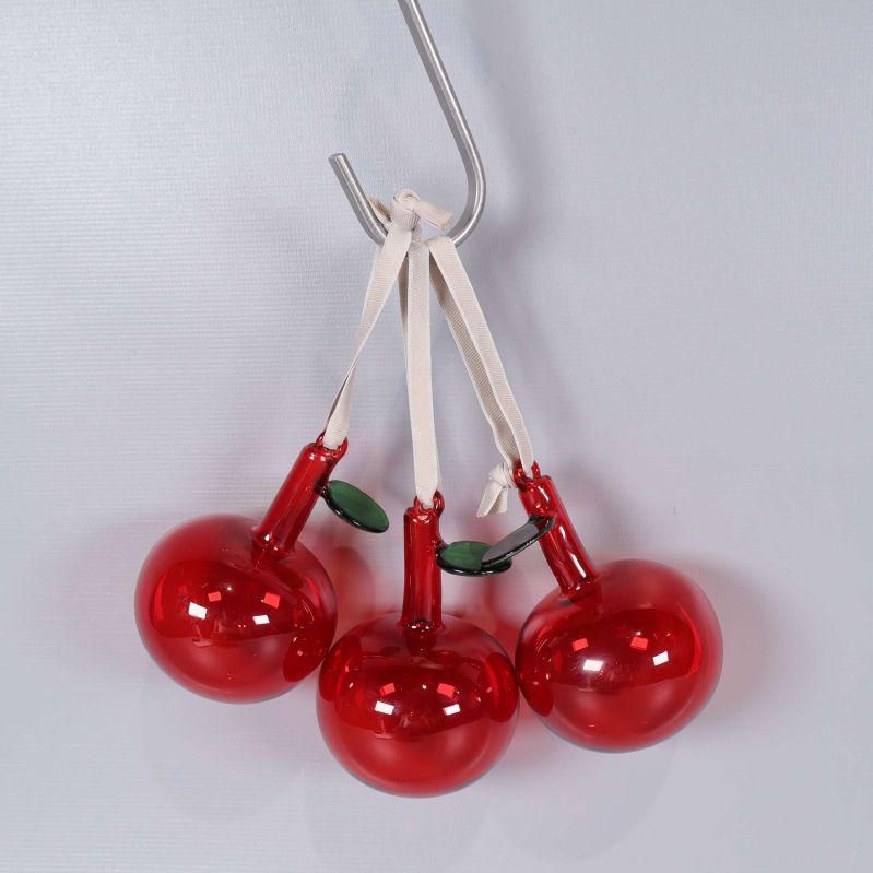 Tre röda glasäpplen hängande i vit snodd