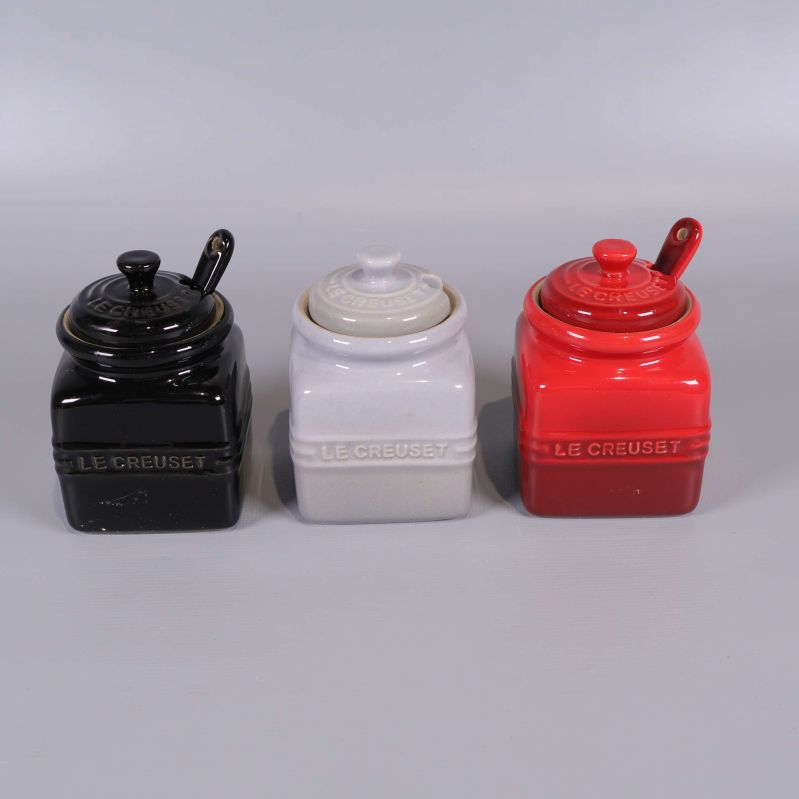 Tre fyrkantiga burkar med lock och sked i svart, vitt och rött