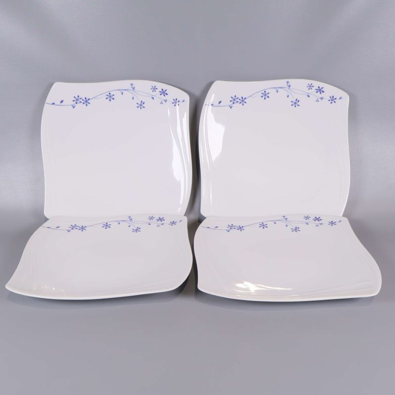 Fyra vita fyrkantiga tallrikar med blå blommönster längs kanten