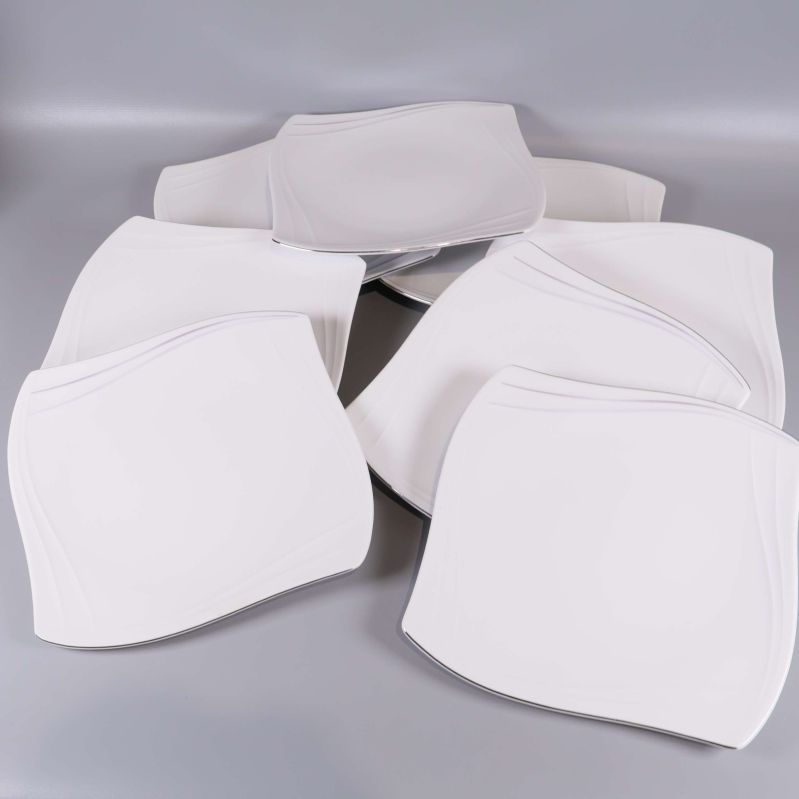 Åtta vita fyrkantiga tallrikar utspridda på grått underlag