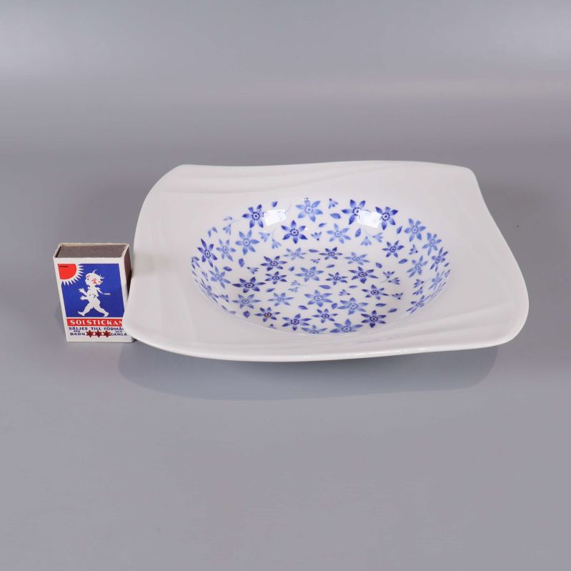 En djup tallrik med blå blommor bredvid tändsticksask