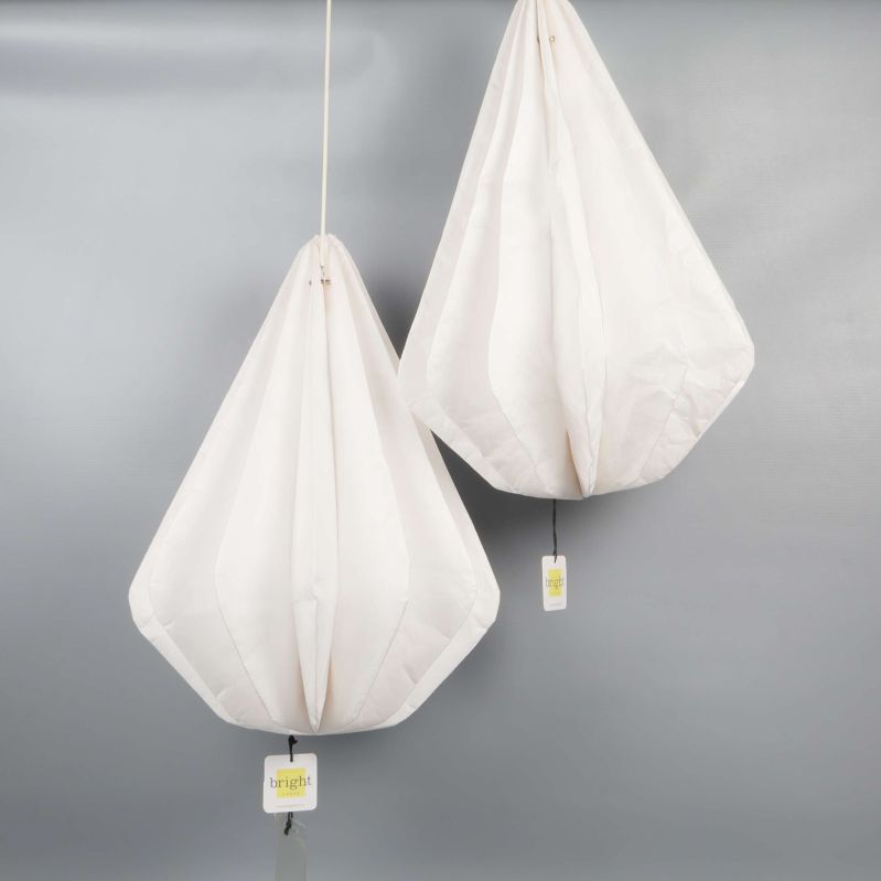 Två vita droppformade lampskärmar hänger mot grå bakgrund