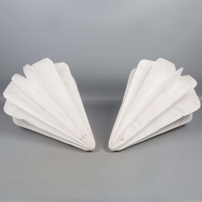 Veckade lampskärmar ligger platta mot grå yta