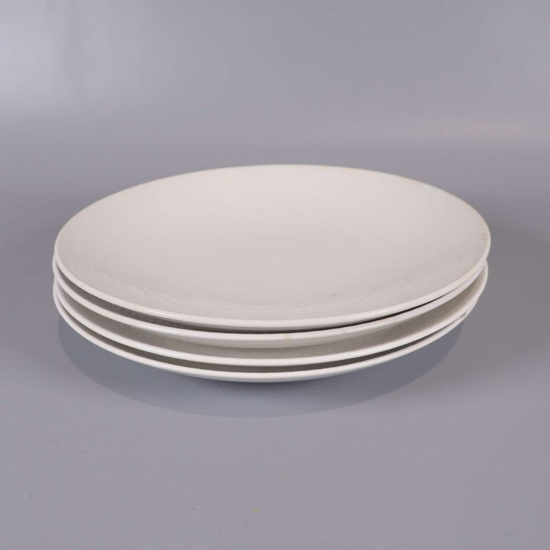 Fyra staplade vita assietter på rad mot grå yta