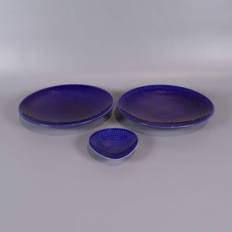 Tre blå serveringsdelar med reliefmönster på grå bakgrund