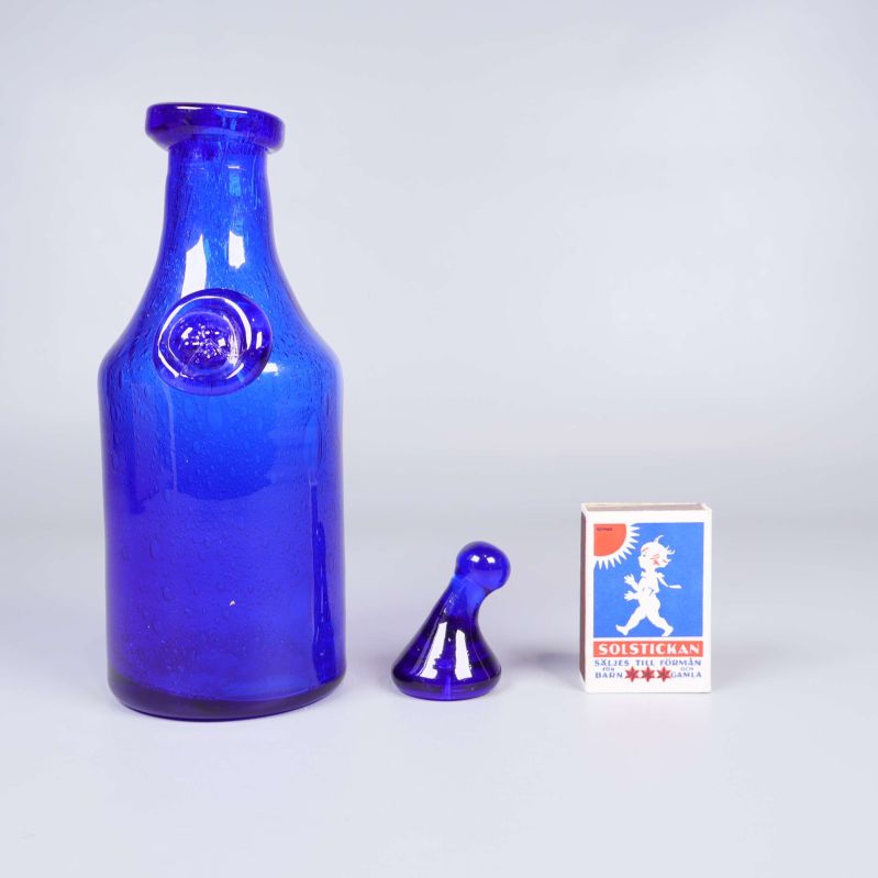 Blå glasflaska med propp samt tändsticksask som storleksreferens