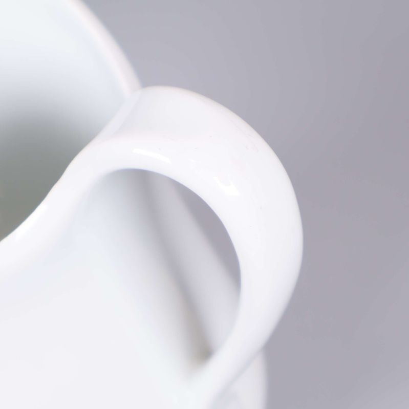 Närbild av vit kannas handtag och glansig yta