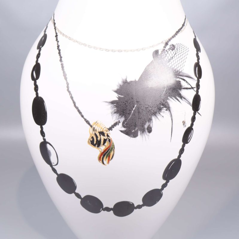 Närbild av motiv på vas med halsband och fjäderdekoration