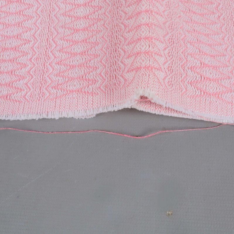 Närbild på tygkant och lösa trådar i ljusrosa tyg