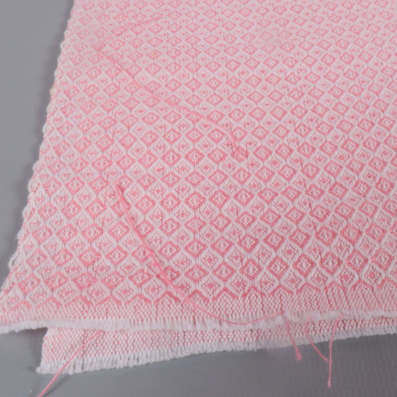 Tyg i ljusrosa med små diamantmönster och lösa trådar