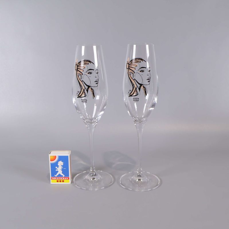 Två champagneglas med ansiktsmotiv jämte tändsticksask