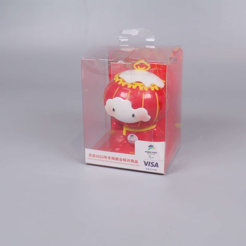 Maskotfigur i vit och röd färg i genomskinlig förpackning sedd snett framifrån