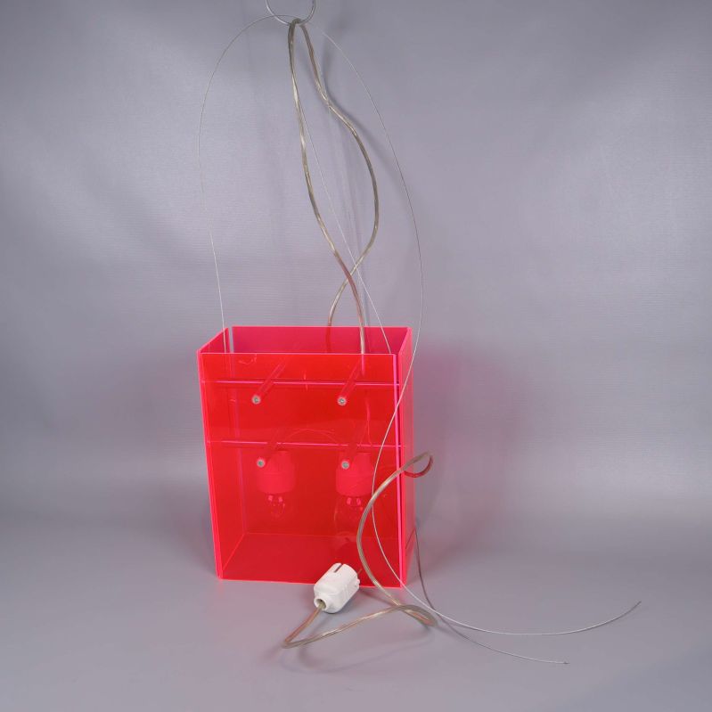 Neonröd lampa med sladdar på golvet sedd snett framifrån