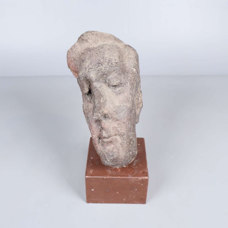 Skulptur av huvud i texturerad sten på brun sockel