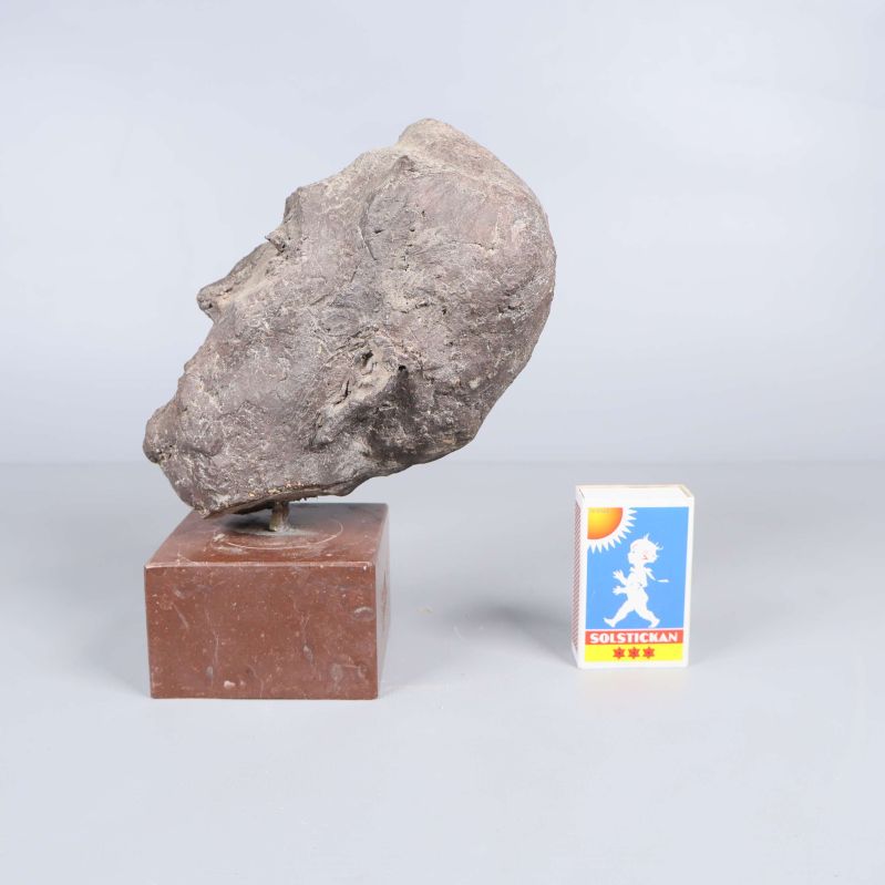 Profilvy av huvudskulptur bredvid tändsticksask för skala