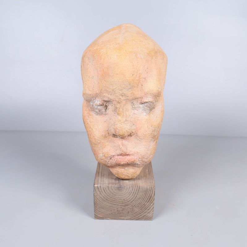 Skulptur av huvud sedd framifrån på träfot