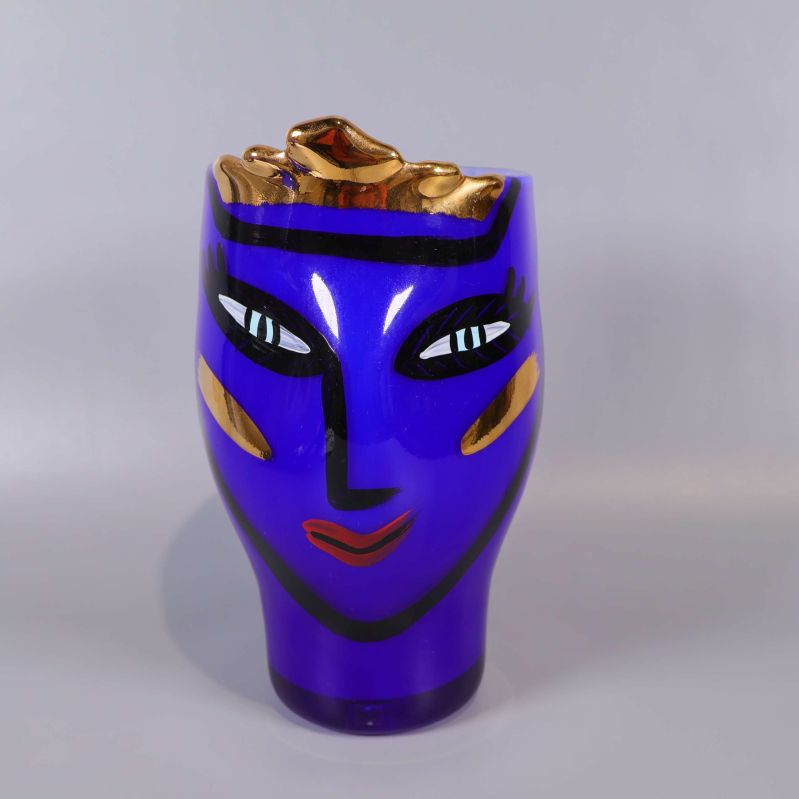 Framsida av blå glasvas med ansiktsmotiv och gulddetaljer