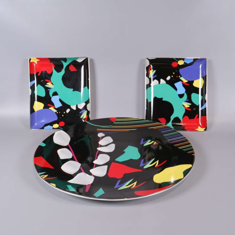 Tre tallrikar med färgglad abstrakt design uppställda mot en grå bakgrund