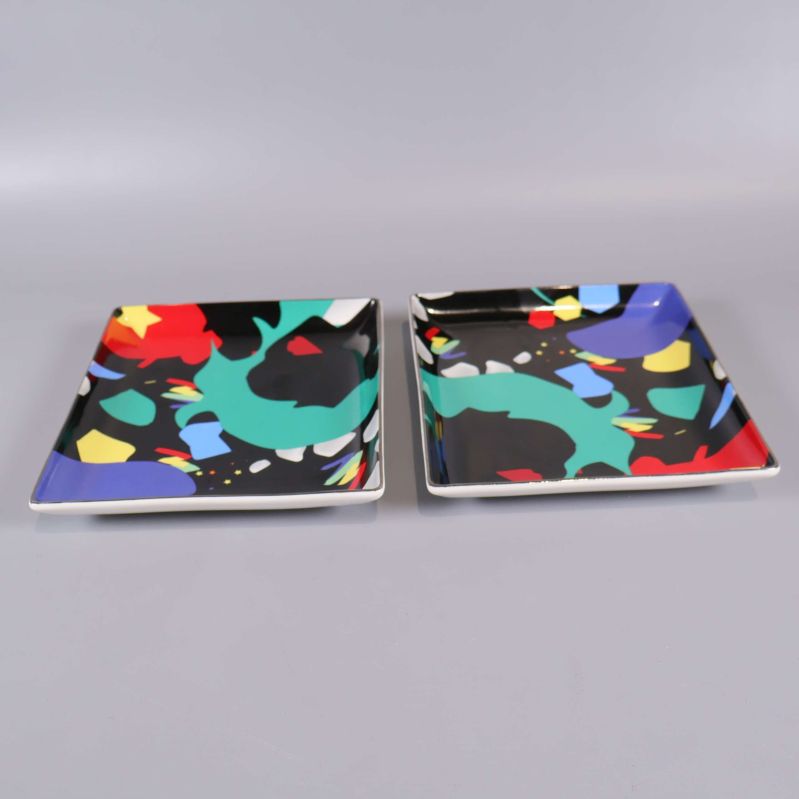 Två fyrkantiga tallrikar med svart bas och färgglada motiv