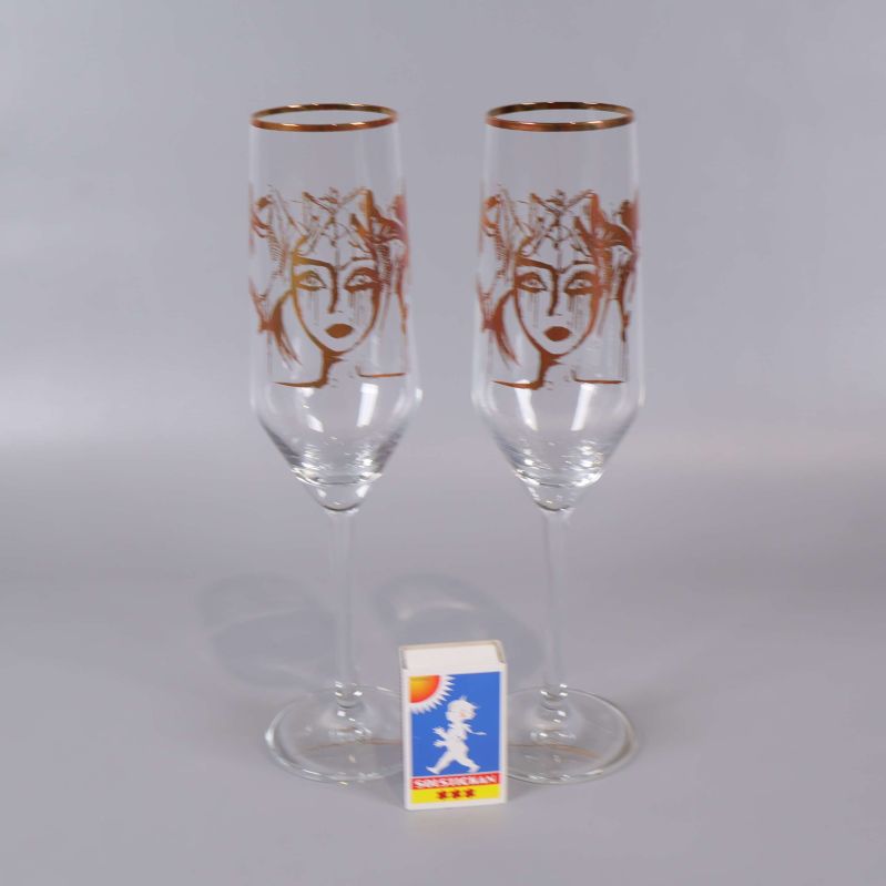Två champagneglas med guldkant och ansiktsmotiv bredvid tändsticksask