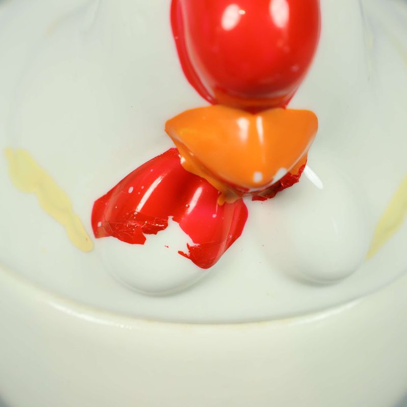 Närbild på röda och orange detaljer på burkens lock med färgbotfall 