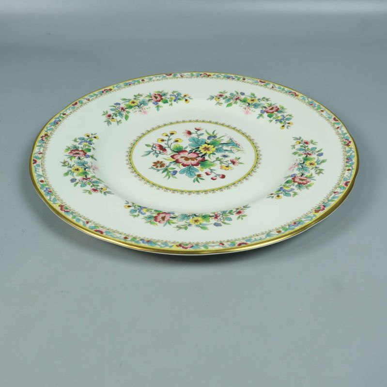 Tallrik med blommigt mönster och guldkant liggande på bord