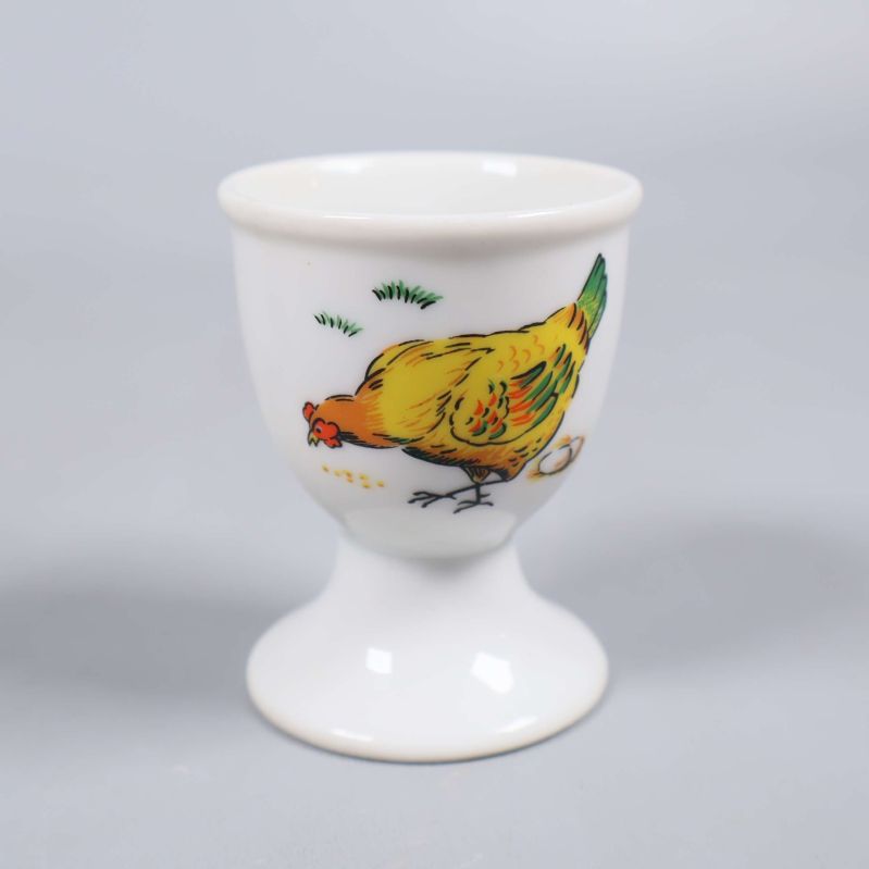 Närbild på vit äggkopp med kycklingmotiv
