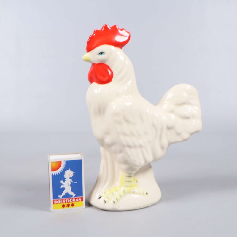 Keramisk tuppfigur bredvid tändsticksask för storleksjämförelse