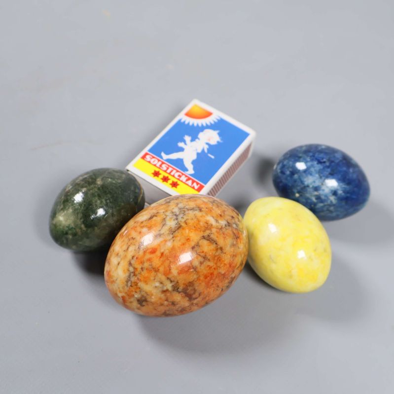 Fyra färgade stenägg och tändsticksask på grått underlag