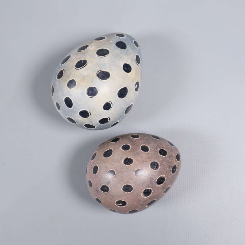 Två äggformade dekorationer med svarta prickar på grå bakgrund