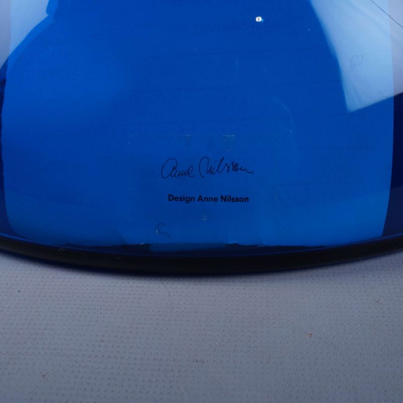 Närbild av signatur och designtext på blå glasvas