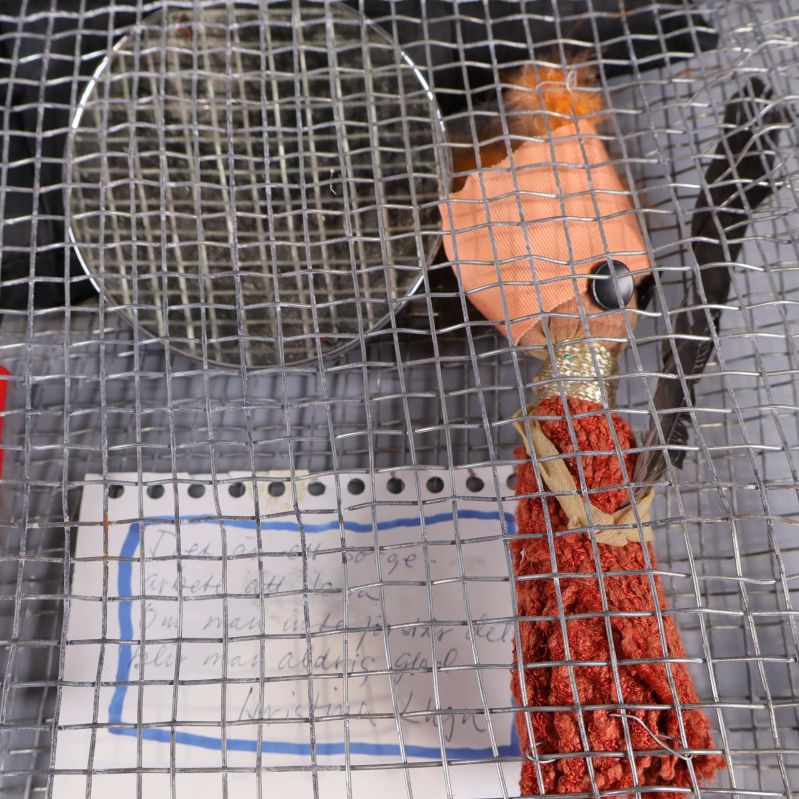 Närbild på figur med orange kropp och papper i nätet