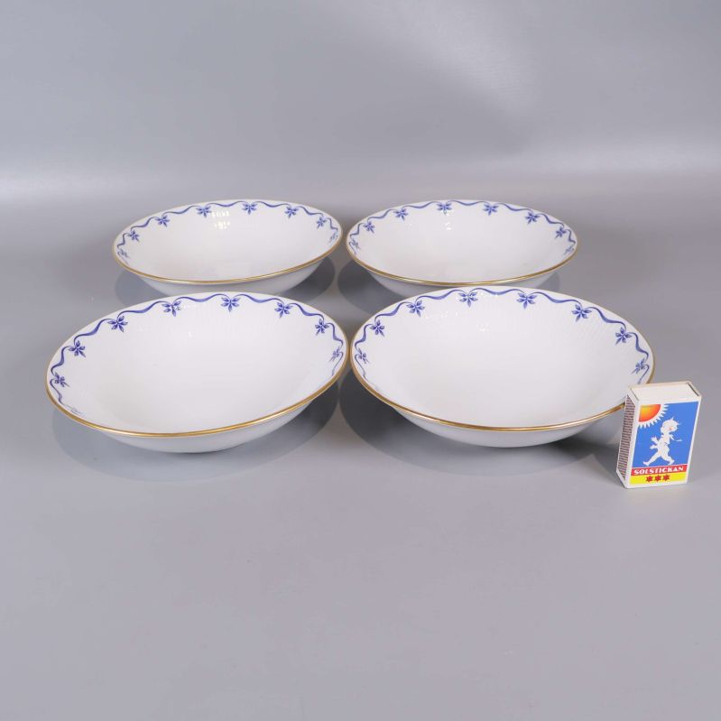 Fyra djupa tallrikar med blå dekor bredvid tändsticksask