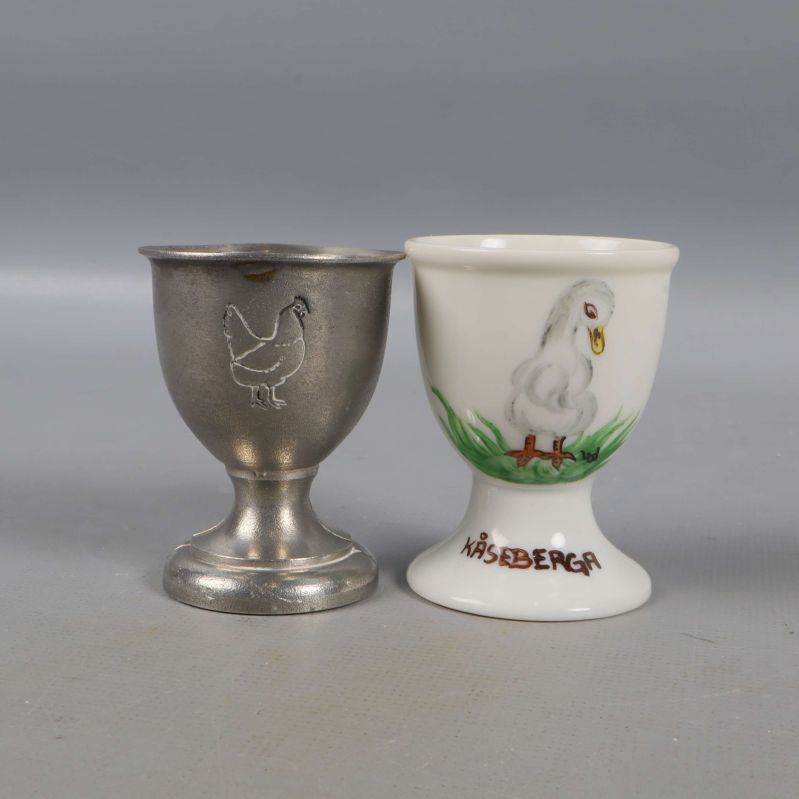 Två ägghållare, en metall en keramik med kycklingmotiv