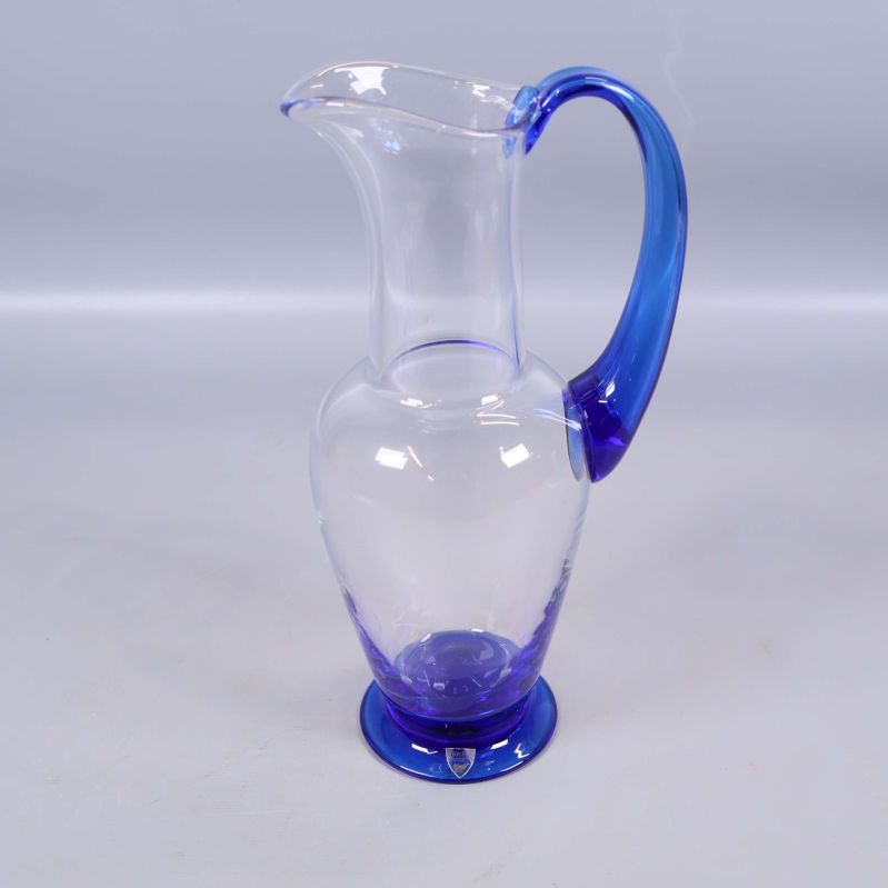 Karaff i klart glas med blå fot och handtag från sned vinkel